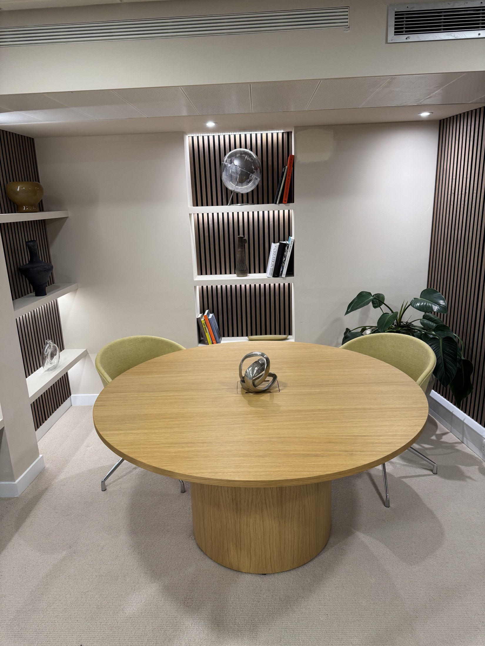 One of the refurbished studio rooms, with a round wooden table, soft green chairs and illuminated display shelves
