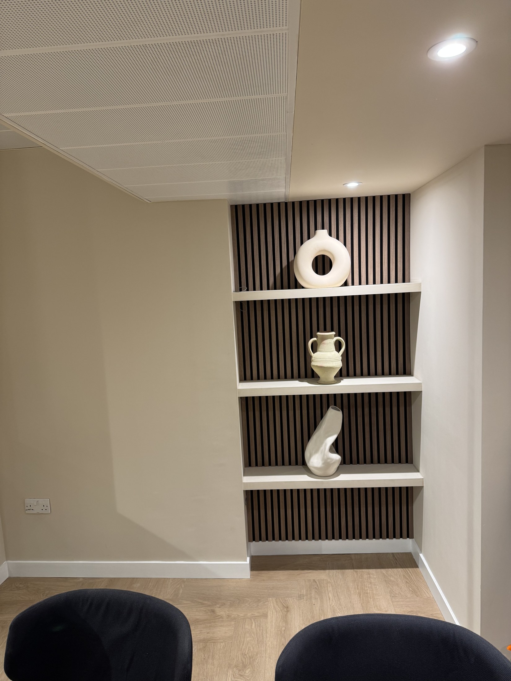 Interior with illuminated shelving, pale ceramics and dark seating