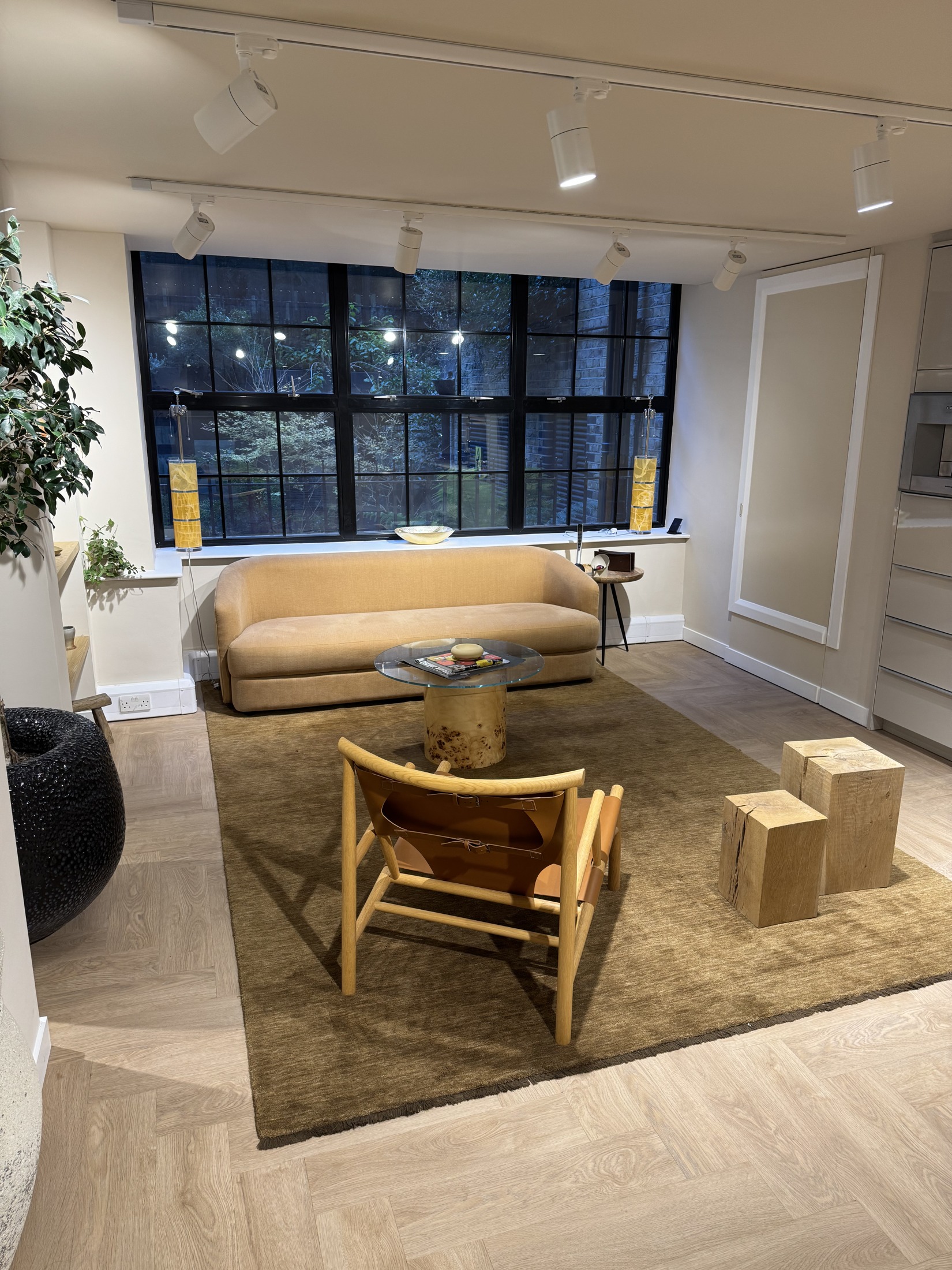 Relaxation area with a pale sofa, leather lounge chair and glass coffee table beside a large courtyard-facing window